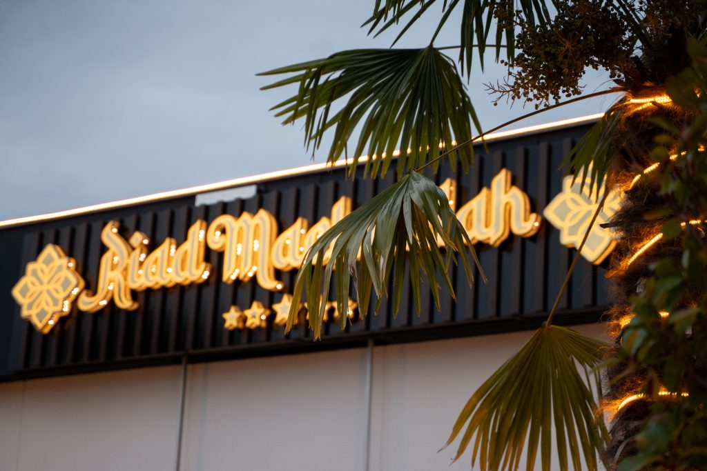 Außenansicht des Riad Mashallah Eventsaals in Karben mit beleuchtetem Logo und Palmen im Abendlicht